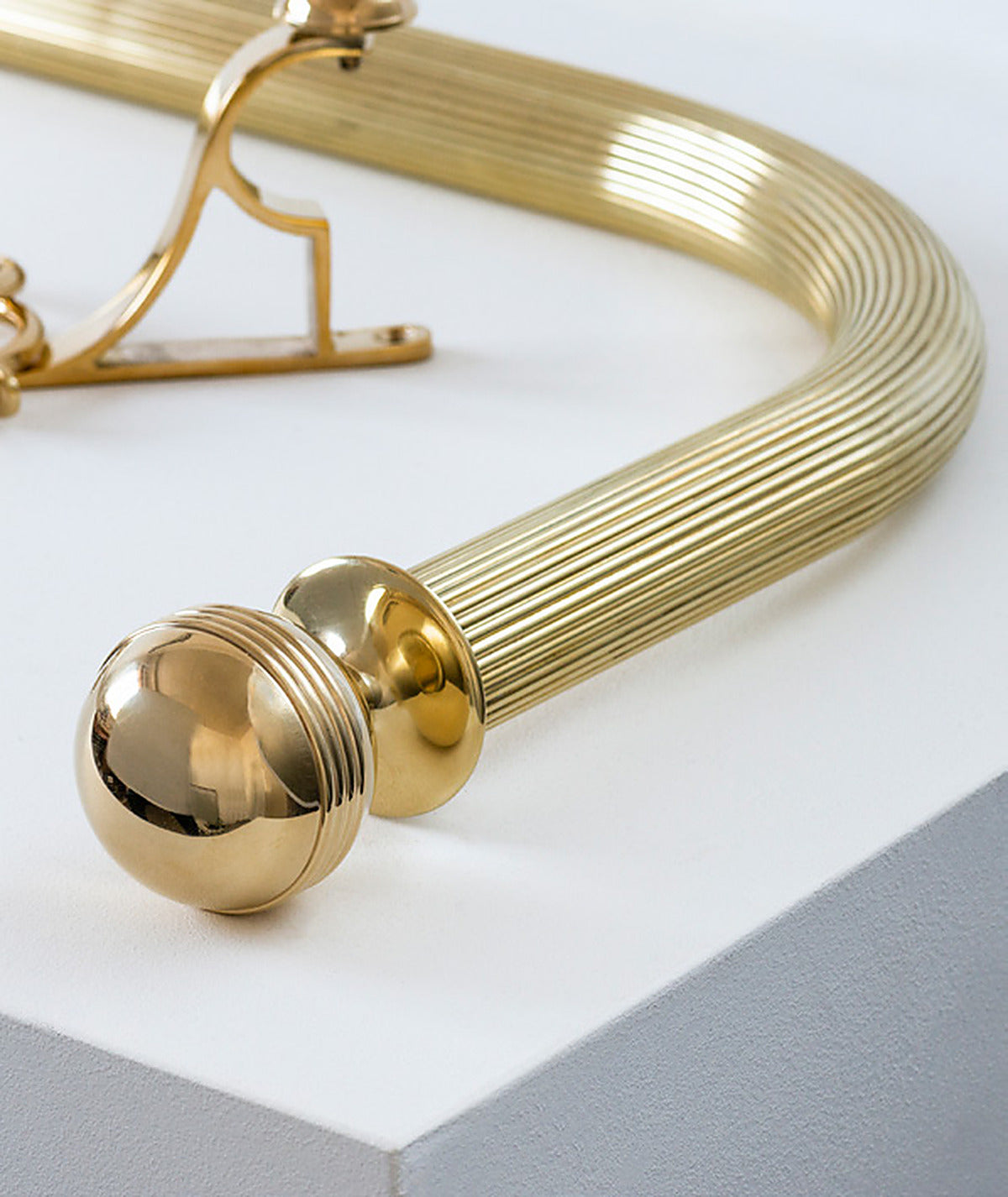 Close-up of the curved bend on a Tillys reeded brass pole with an adjustable bracket and ball finials
