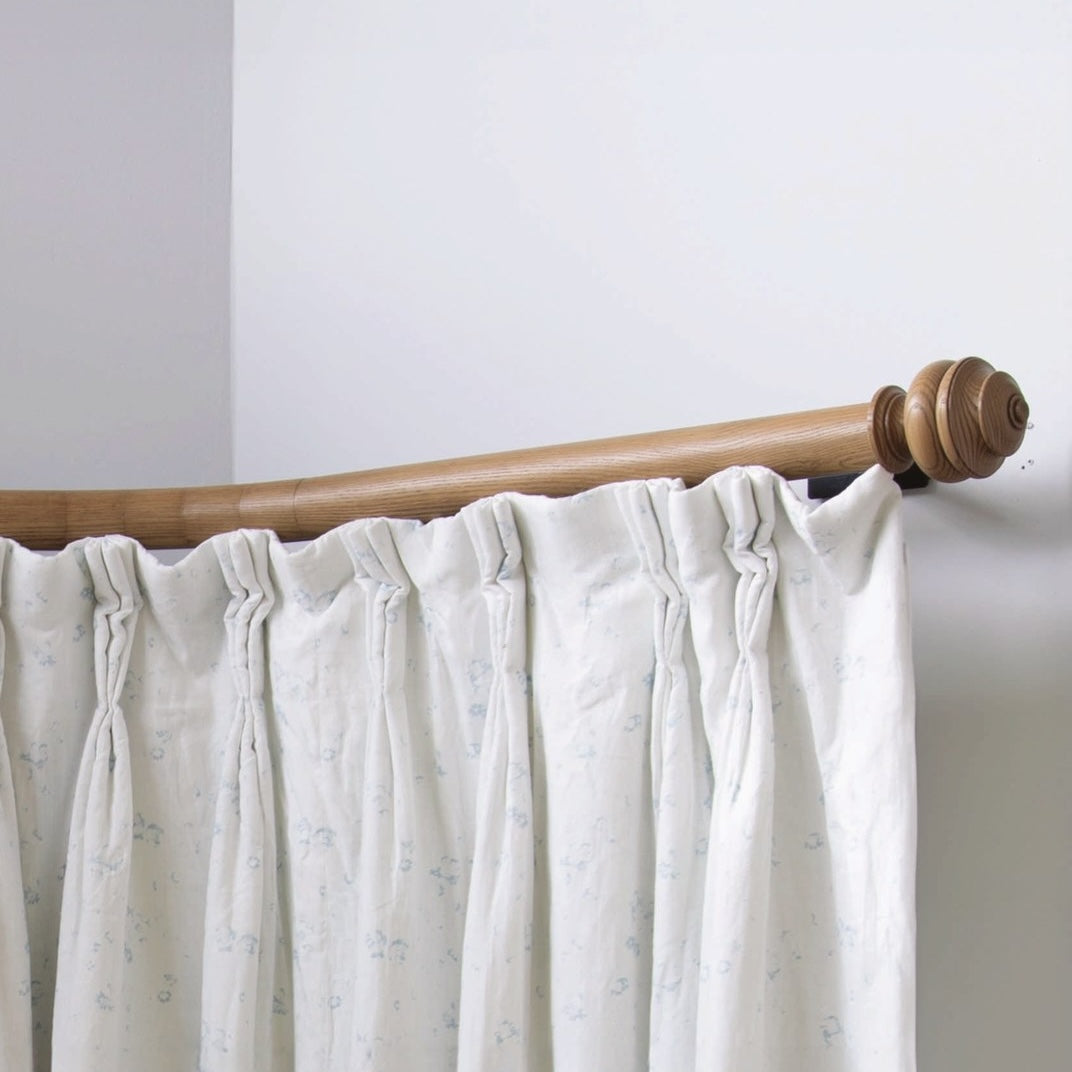 Byron &amp; Byron wooden bay window curtain pole in oak, bent round the corner of a bay with cream curtains